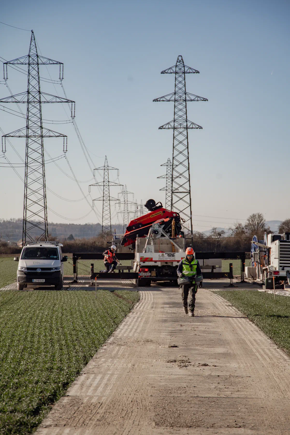 Bauarbeiter geht auf Behelfsstraße zur Baustelle bei Strommasten.