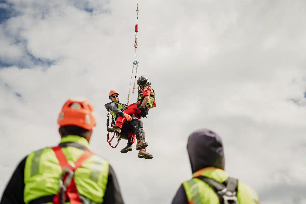 Arbeiter im Helikopter-Lastenseil hängend bei der Montage an einem Strommast.